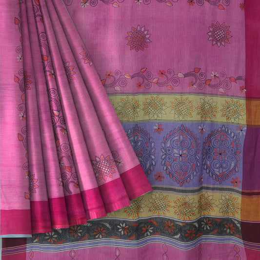 A pink patterned fabric, likely a saree or scarf, draped to show both the body and the border. The fabric features hand-drawn style floral and paisley motifs in pink, purple, yellow, and orange, with a solid magenta border and a decorative multicolor patterned edge.