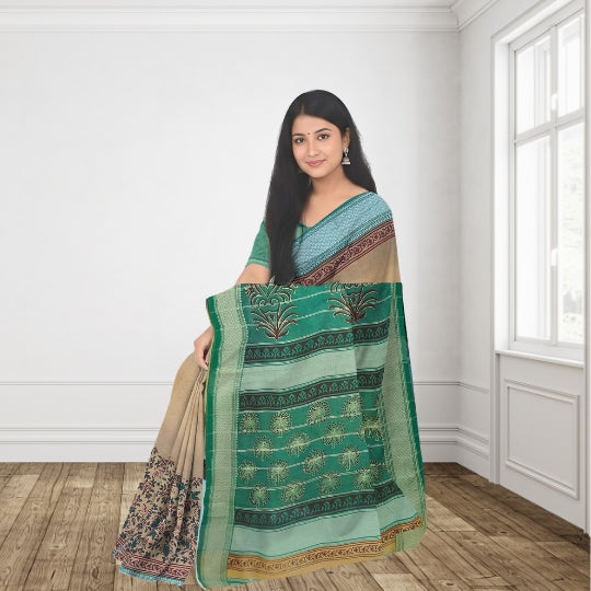 A woman models a green and beige patterned saree in a bright room with white walls and wooden floors. The saree features a green body with printed motifs, a beige border, and a teal blouse.