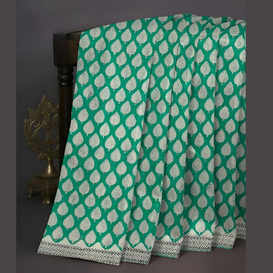 A green and white printed fabric, likely a saree or scarf, draped over a dark wooden stand. The fabric features a repeating white teardrop block print pattern on a vibrant green base, with a decorative border at the bottom.