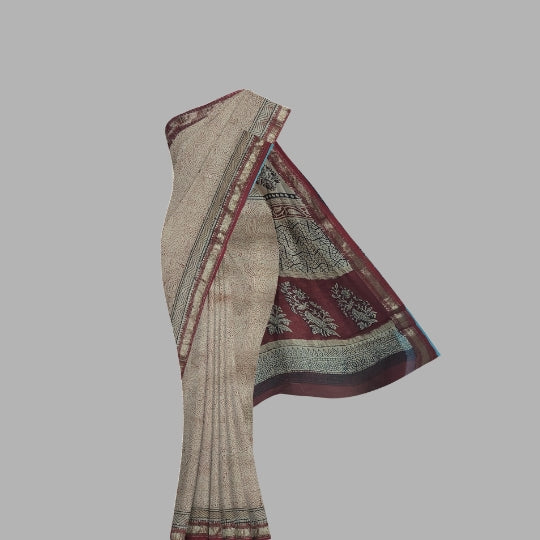 A draped saree with a beige body, deep red border, and detailed black and gold zari patterns, shown against a solid gray background.