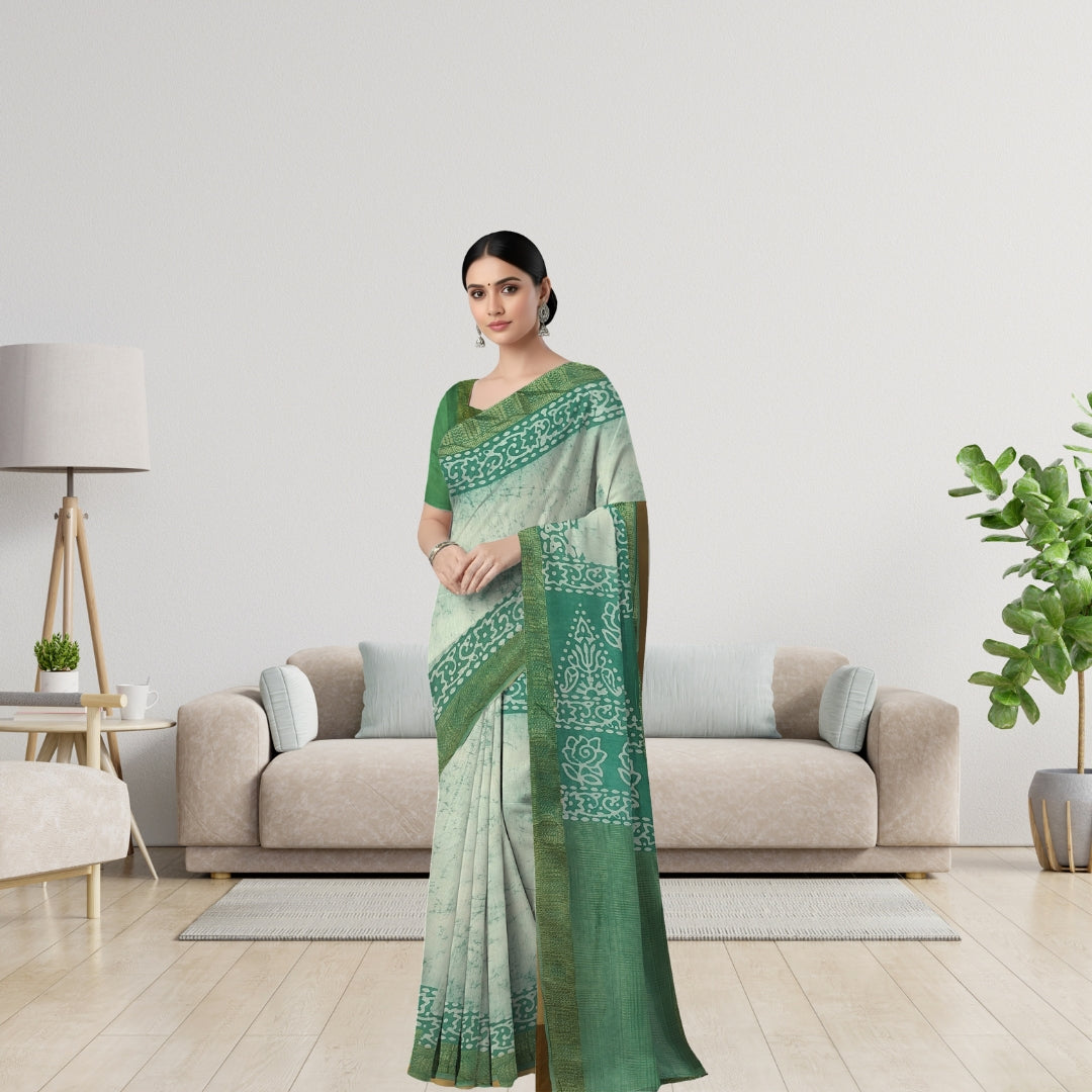 A woman modeling a green and white patterned saree in a modern living room setting with a beige sofa, wooden floor, and potted plants.