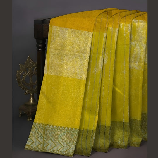 A draped yellow and gold saree with a patterned border, displayed on a dark wooden stand against a dark gray background.