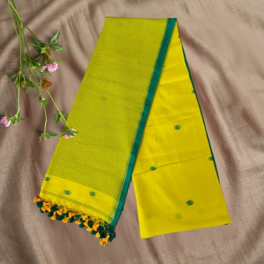 A folded yellow and green saree or fabric piece displayed on a beige fabric background, with small pink flowers placed along the left side.