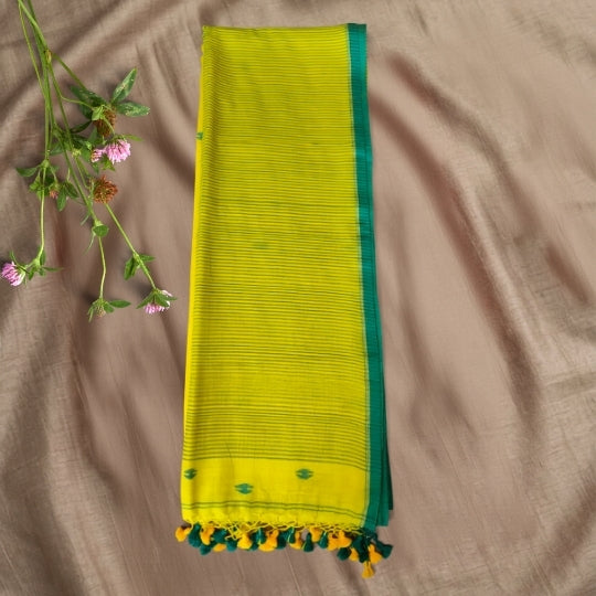 A folded lime green and dark green saree or fabric piece with a striped body and tassels, laid flat on a beige fabric background with a small sprig of flowers at the upper left.